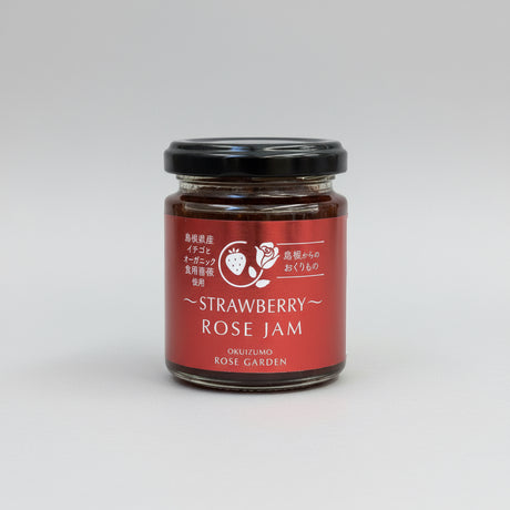 A jar of Okuizumo Rose Garden strawberry rose jam with label in Japanese and English, placed on a wooden surface.
