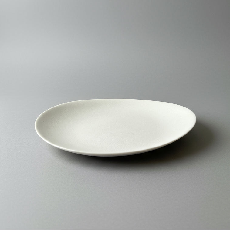 A white oval-shaped porcelain tea plate displayed on a wooden surface.